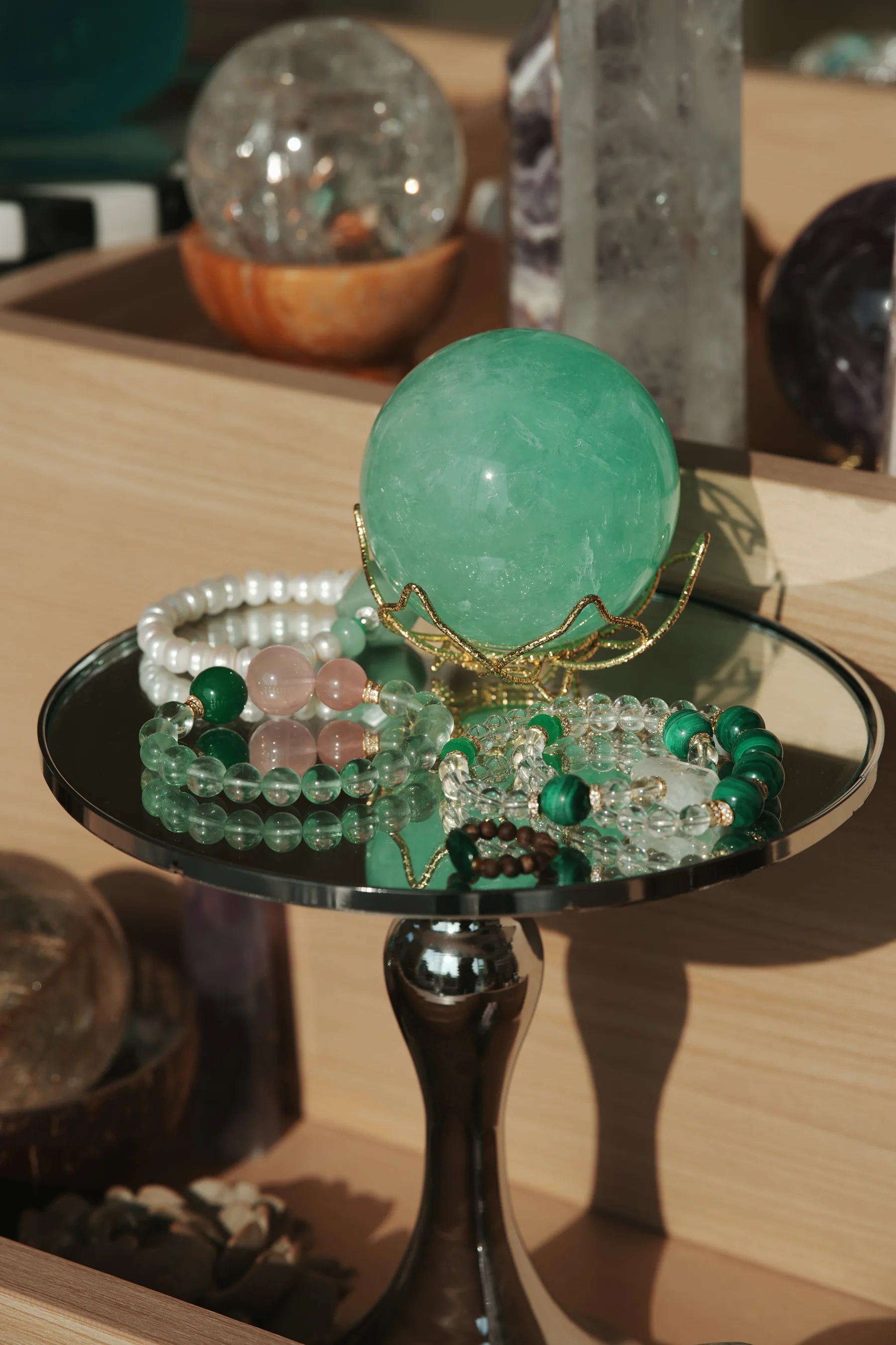 A green crystal sphere and crystal bracelets displayed together on a mirrored stand